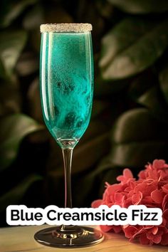 a blue creamsice fizz is sitting on a table next to some flowers