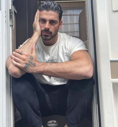 a man sitting in the doorway of a van with his hand on his head and looking at the camera