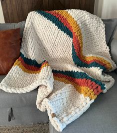 a couch with a blanket on top of it next to a pillow and brown pillow