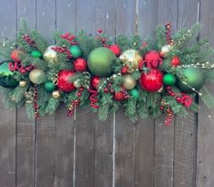 a long christmas garland with ornaments hanging from it's sides on a wooden fence