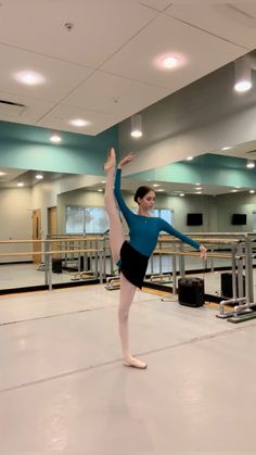 a young ballerina is practicing her moves in an empty room with lights on the ceiling