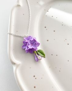 a purple flower on a silver chain is sitting on a white plate, with dots around it