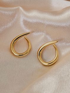 two pairs of gold hoop earrings sitting on top of a white cloth