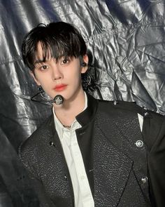 a young man wearing a black jacket and white shirt is posing in front of a silver background