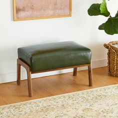 a green leather bench sitting on top of a hard wood floor next to a potted plant