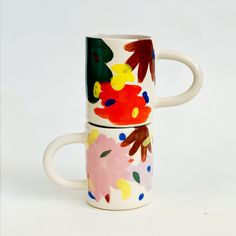 two coffee mugs sitting side by side on top of each other, one with flowers painted on it