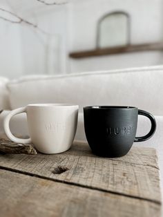 two black and white coffee cups sitting on top of a wooden table next to each other