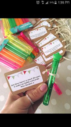 a hand holding a green pen next to some small tags with writing on them and paper clips