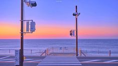 an empty parking lot next to the ocean at sunset or sunrise with traffic signals and street lights