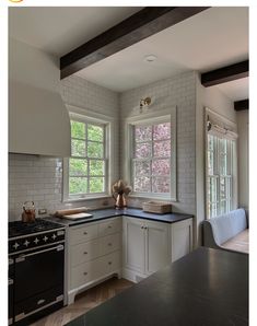 a kitchen with white cabinets and black counter tops next to a stove top oven in front of two windows