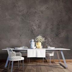 a dining table with two chairs and a vase on it, in front of a concrete wall