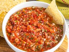 a white bowl filled with salsa and tortilla chips on top of a wooden cutting board