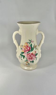 a white vase with pink flowers painted on the side and green leaves in the middle