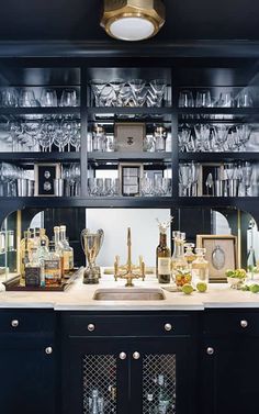 a kitchen counter with wine glasses and liquor bottles on the shelves above it is an old fashioned clock