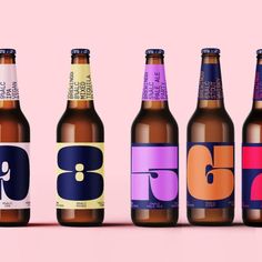 six different beer bottles are lined up on a pink and blue background, with the same color as the bottle