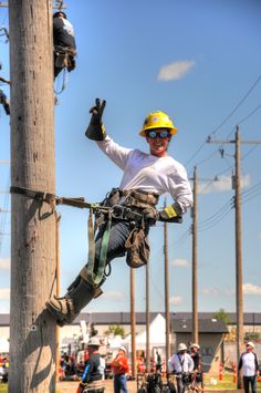 a man in safety gear hanging from a telephone pole with his hand up to the ground