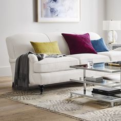 a living room with white couches and colorful pillows on the table in front of it