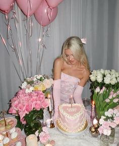 a woman sitting in front of a pink cake with candles on it and balloons behind her