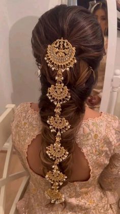 a woman with long hair in a braid and gold jewelry on her head is looking into the mirror