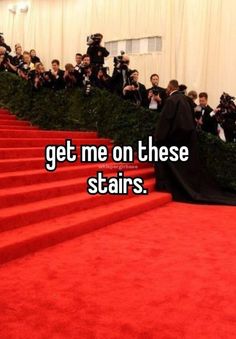 a woman in a black dress standing on the stairs with people taking pictures behind her