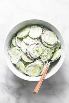 cucumber salad in a white bowl with a wooden utensil on the side