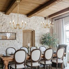 a dining room table with chairs and a chandelier hanging from the ceiling in front of a stone wall