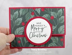 a hand holding up a christmas card with holly leaves on it and merry little christmas