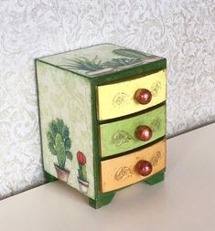 a small green and yellow drawer with plants painted on the drawers, sitting on a table