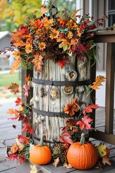 a wooden barrel filled with fall leaves and pumpkins on top of a porch table