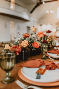 the table is set with orange and white plates, napkins, and vases