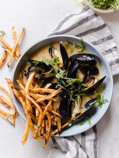 a bowl filled with mussels and fries on top of a white table cloth