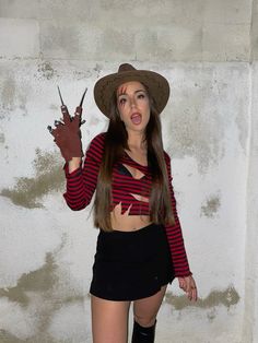 a woman with long hair wearing a hat and holding scissors in one hand while standing next to a wall