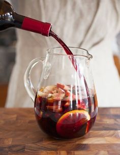 a person pouring red wine into a pitcher filled with fruit