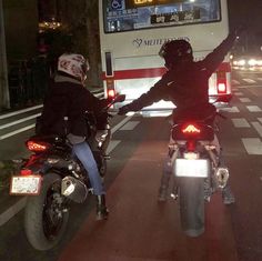 two motorcyclists riding down the street at night with their arms in the air