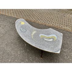 a metal bench sitting on the side of a road next to a brick sidewalk and cobblestone walkway