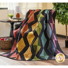 a multicolored quilt sitting on top of a wooden floor next to a potted plant