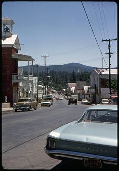 an old time town with cars parked on the side of the road and mountains in the background