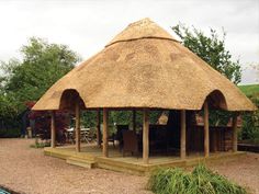 a thatched roof gazebo in a gravel area with tables and chairs around it