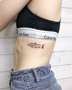 a woman with a fish tattoo on her stomach is standing in front of a white wall