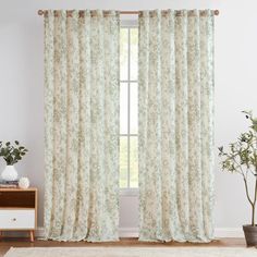 a living room with a white rug and window covered in floral print curtain panels next to a potted plant