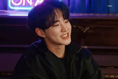 a young man sitting at a piano in front of a neon sign that reads one