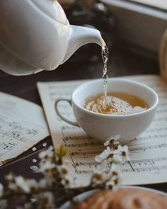 tea being poured into a white cup on top of an open book with music sheets