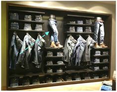 a large display case filled with lots of jeans and jackets on wooden shelves in front of a wall