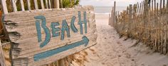 a wooden sign that says beach next to a fence on the beach near the ocean