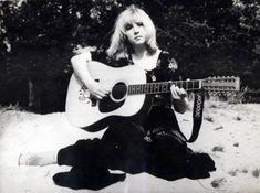 a black and white photo of a woman sitting in the sand with an acoustic guitar