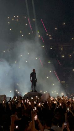 a man standing on top of a large rock surrounded by lots of people holding up their cell phones