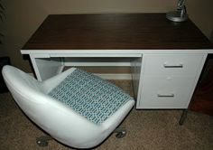 a white chair sitting next to a desk with a blue pillow on top of it