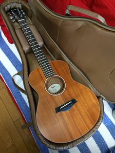 an acoustic guitar sits in its case on top of a striped blanket with a red, white and blue pillow