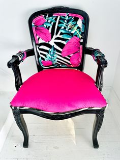 a black chair with pink and blue flowers on the back is against a white wall