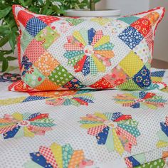 a colorful quilted bed with two pillows on it and a potted plant in the background